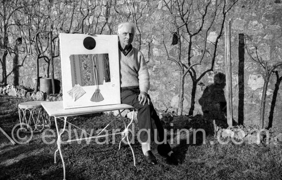Max Ernst in the garden of her house at Seillans 1966. He holds the painting Schmetterling-Steuerzahler (papillon contribuable), for which he has used a piece of wallpaper, a flybat and a note from the income tax officer concerning his income tax return. - Photo by Edward Quinn