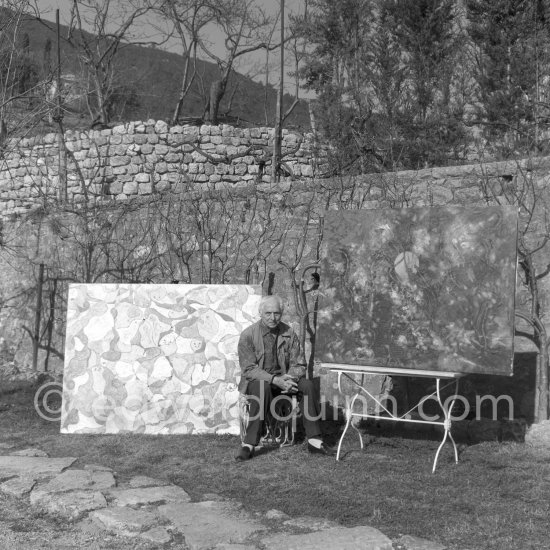 Max Ernst in the garden of his home with "Das Fest in Seillans" ("La fête à Seillans") and on the right "Der letzte Wald" ("La dernière forêt") first version, 1960-1969. Seillans 1966. - Photo by Edward Quinn