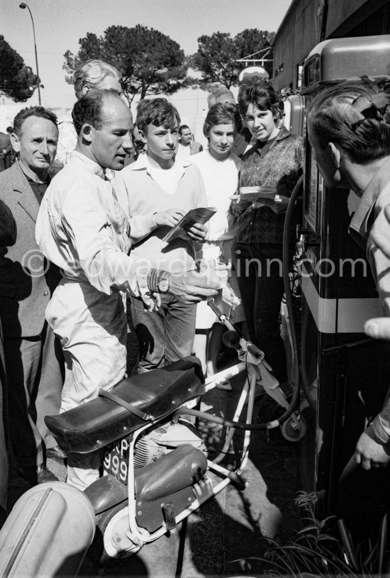 Stirling Moss signing autographs. He enjoys riding around with his 1961 Trojan Trobike. Monaco Grand Prix 1961. - Photo by Edward Quinn
