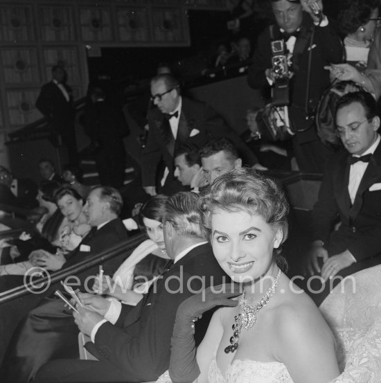 A close-up on Sophia Loren and her exceptional necklace. Present at the gala Evening at the Palais du Festival were also Silvana Mangano (partly hidden) and her husband Dino de Laurentiis (on the right, eyes closed). Cannes 1955. - Photo by Edward Quinn