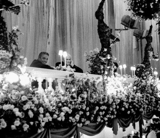 Aristotle Onassis and George Embiricos, another greek ship magnate watching the party from the balcony. "Bal de la Rose" gala dinner at the International Sporting Club in Monte Carlo, 1958. - Photo by Edward Quinn