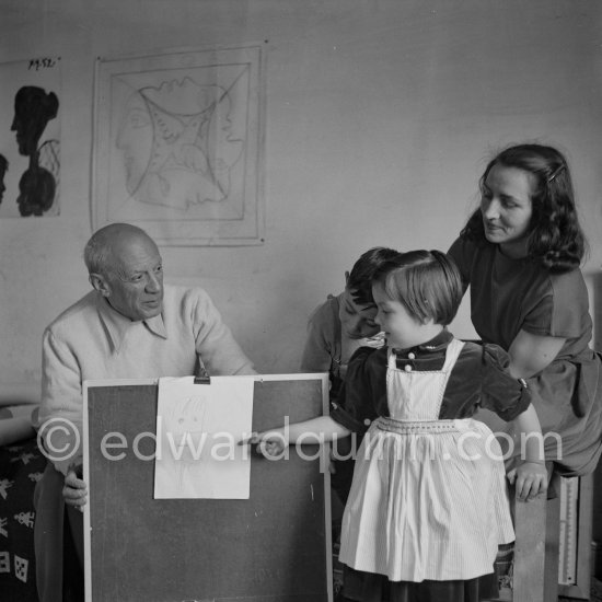 Encouraged by his father, Claude Picasso tries to do a portrait of Pablo Picasso, portraying him with a round face, deep furrows on his forehead, a triangle for a nose, and streaks of hair on the sides of his head. La Galloise, Vallauris 16.4.1953. - Photo by Edward Quinn