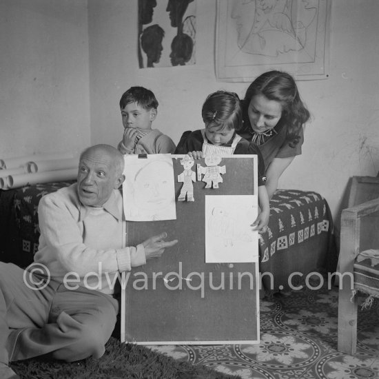 Encouraged by his father, Claude Picasso tries to do a portrait of Pablo Picasso, portraying him with a round face, deep furrows on his forehead, a triangle for a nose, and streaks of hair on the sides of his head. La Galloise, Vallauris 16.4.1953. - Photo by Edward Quinn