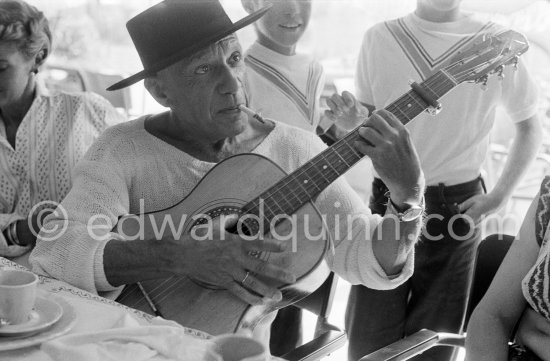 In Spanish mood Pablo Picasso wears a "chapeau cordouan" as he pretends to play guitar at restaurant Le Vallauris. Vallauris 11.8.1955. - Photo by Edward Quinn