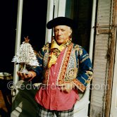 Pablo Picasso in a whimsical costume. Among other things, he has on a bullfighter’s jacket, given to him by his friend, the famous matador Dominguin. In front of the garden gate at La Californie. Cannes 1956. - Photo by Edward Quinn