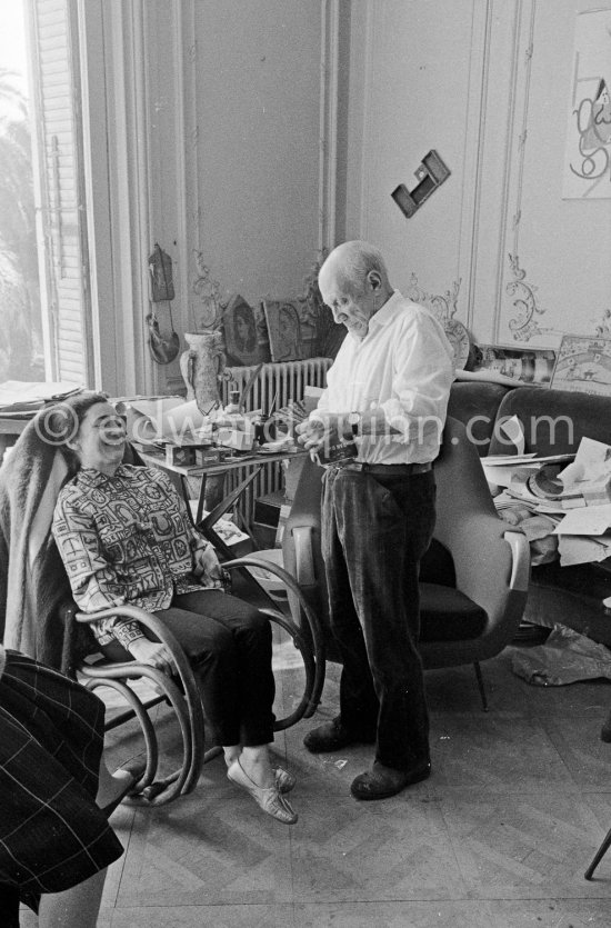 Pablo Picasso and Jacqueline. Jacqueline, sitting in a rocking chair, is wearing a blouse made from a textile designed by Pablo Picasso. La Californie, Cannes 1961. - Photo by Edward Quinn