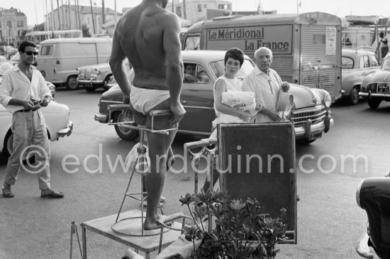 Pablo Picasso and Catherine Hutin looking at an artist who is posing for the promotion of a circus. Quai Gabriel Péri, Port de Saint-Tropez 1961. - Photo by Edward Quinn